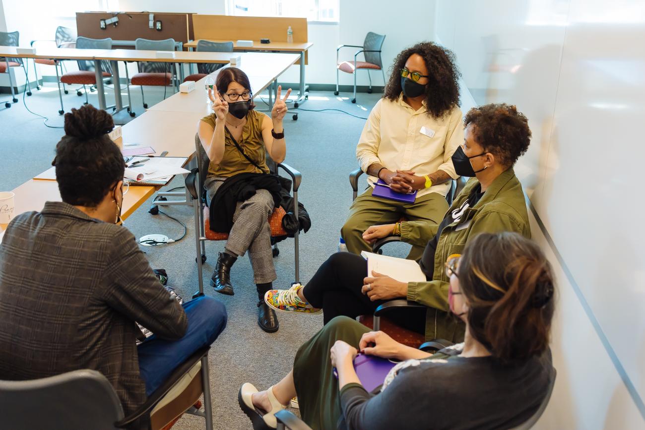 group of people in masks indoors having a discussion in a circle